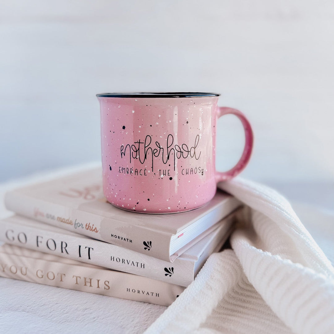Pink mug with text on a stack of books with motivational quotes