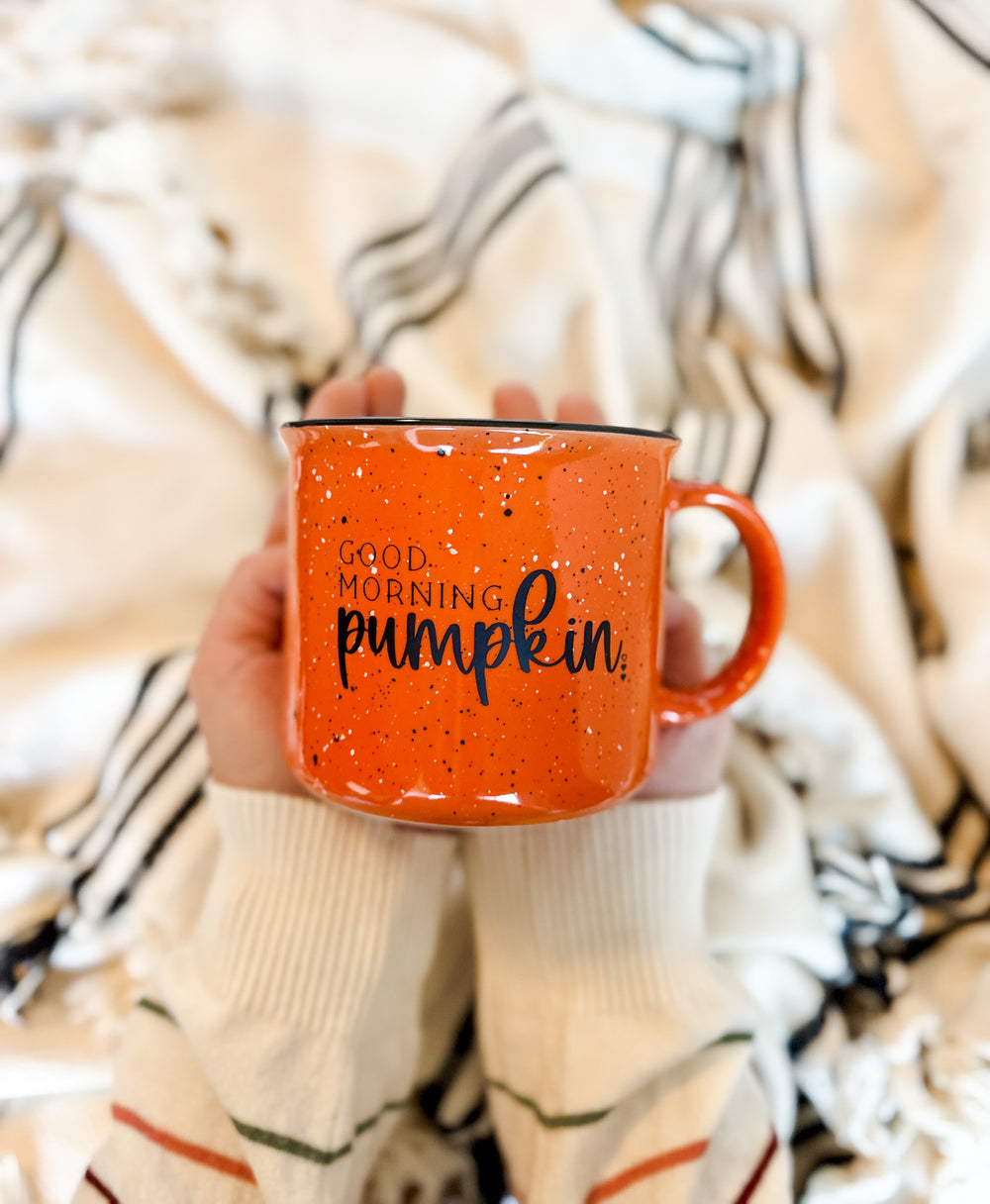 Orange mug with 'Good Morning Pumpkin' text held by a person against a cozy blanket background