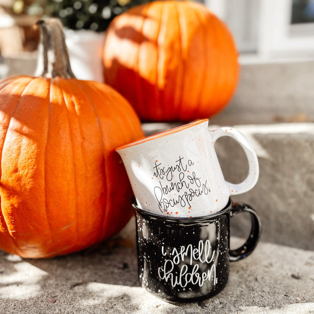 Two mugs with autumn-themed text on a stone surface with pumpkins in the background.