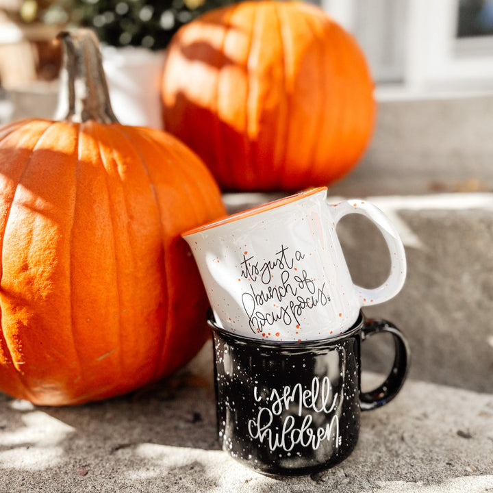 Two mugs with autumn-themed text on a stone surface with pumpkins in the background.