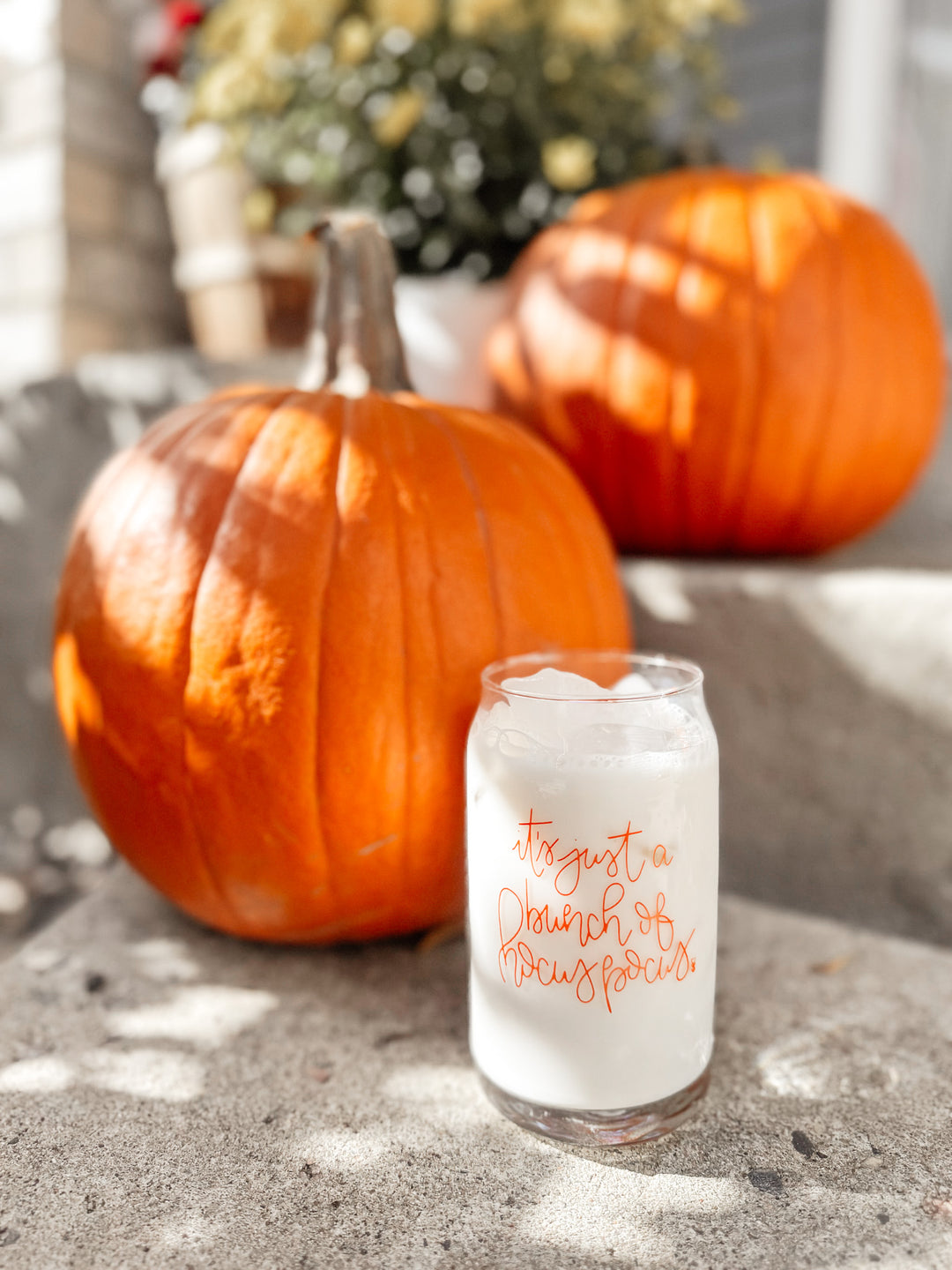 Glass of iced drink with text next to pumpkins on a stone surface